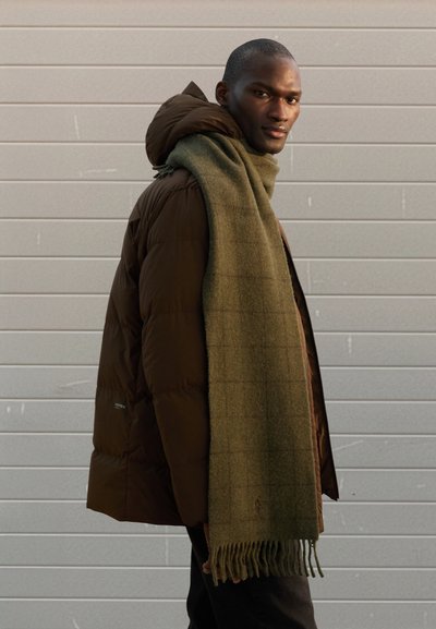 Brun puffjakke med hette, kombinert med et mørkegrønt skjerf med rutenettsmønster. Slank passform og teksturert stoff.