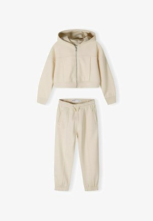 Haut hoodie beige court avec fermeture éclair à l'avant et poche kangourou, associé à un pantalon ajusté assorti avec une ceinture élastique et des poches latérales.