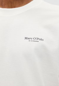 Λευκό πουκάμισο με γύρο λαιμό και μικρό μαύρο λογότυπο "Marc O’Polo EST. IN STOCKHOLM" στο αριστερό στήθος.