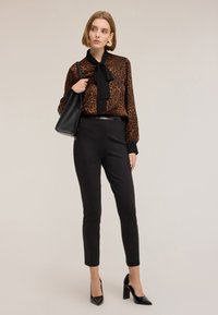 Bluzka w leo wzór z czarnym kołnierzykiem i kokardą, noszona ze dopasowanymi czarnymi spodniami i czarnymi szpilkami. Czarna torebka na ramię jako dodatek.