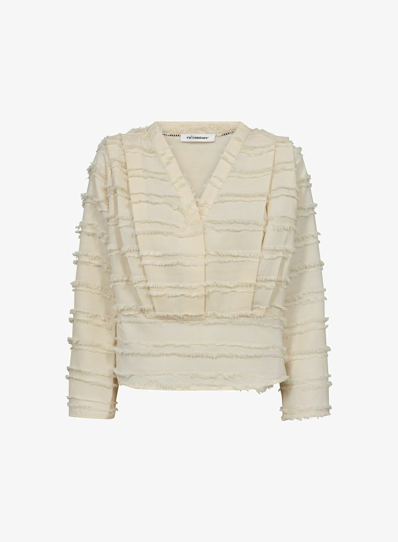 Kreminės spalvos palaidinė su V formos iškirpte, puošta sluoksniuotais volanais visoje medžiagoje. Ilgos rankovės ir trumpesnis fasonas su tekstūruota medžiaga.