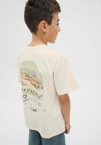 Helles beige Baumwoll-T-Shirt mit einem Retro-Grafikdesign, das im Hintergrund ein oranges Auto und eine Küstenlandschaft zeigt. Kurze Ärmel, Rundhalsausschnitt.