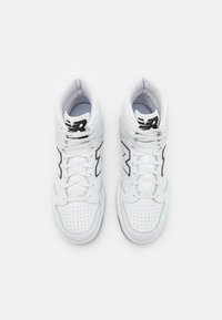 Weiße hochschnittige Sportschuhe mit perforierten Details, schwarzen Logo-Akzenten und einer strukturierten Sohle. Die Schnürsenkel sind durch Ösen gefädelt für einen sicheren Sitz.