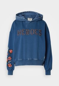 Μπλε βαμβακερή φούτερ με κουκούλα, που έχει την επιγραφή "HEROES" με μεγάλα γράμματα στο μπροστινό μέρος και λουλουδάτη κεντημένη λεπτομέρεια σε έναν ώμο.