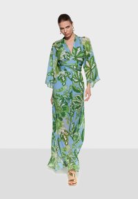 Maxi dress in light blue chiffon featuring a green floral pattern, wrap design, and long, flowing sleeves. Gold sandals complement the look.