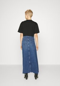 Fekete, rövid ujjú, cropped póló, amely egy hosszú kék farmer szoknyával van párosítva, hátoldali zsebekkel és középső varrással, hátulról látható.