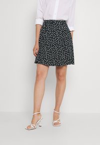 Jupe noire avec des pois blancs, design évasé, tissu léger et ceinture. Associée à des sandales à talons hauts blanches à lanières.