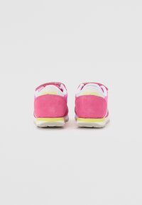 Baskets en daim rose avec des accents blancs et jaunes. Le talon arbore la marque "Saucony". Forme arrondie avec une semelle texturée. Matériaux doux utilisés.