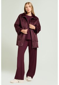 Bordeaux-rød fleecejakke med højt krave, sidelommer og lynlåslukning foran. Kombineret med matchende løstsiddende bukser og lyse sneakers.