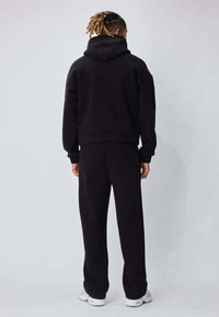 Ensemble sweat à capuche et pantalon de survêtement noirs en tissu doux, avec une coupe décontractée, des poignets côtelés et une poche kangourou à l'avant.