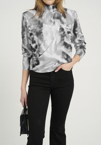 Blusa astratta grigia e bianca con colletto alto e maniche lunghe, abbinata a pantaloni neri e a una borsa nera strutturata.