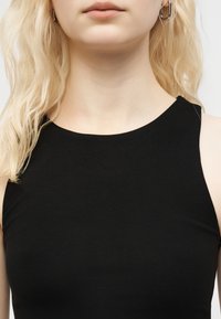 Ξανθιά γυναίκα που φοράει ασημένια σκουλαρίκια κρίκους και μαύρο αμάνικο τοπ, με τα μαλλιά της να πέφτουν στον αριστερό της ώμο.