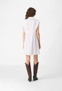 Λευκό φόρεμα χωρίς μανίκια με γιακά, με εφαρμοστή σιλουέτα και πλαινές ραφές, συνδυασμένο με καφέ καουμπόικες μπότες μέχρι το γόνατο με μυτερή μύτη.