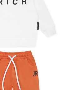 Biała bluza z kapturem z napisem "RICH" w kolorze czarnym, zestawiona z pomarańczowymi dresami posiadającymi elastyczny pas i kieszeń boczną.
