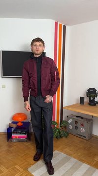 Casaco bomber burgundy com punhos canelados, fecho de zip, e bolso lateral, usado sobre um suéter de gola alta preto; combinado com jeans largos escuros e sapatos castanhos.