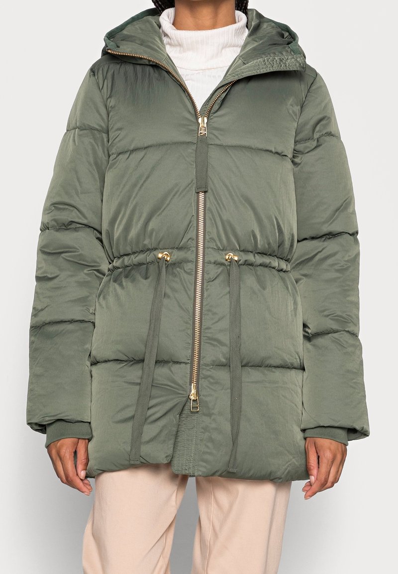 Ljusgrön pufferjacka med huva, guldmed dragkedjor, snörning i midjan och ribbade ärmslut. Har en slät, något glänsande textur.