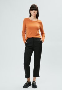 Suéter naranja de punto con un cuello redondeado, combinado con pantalones negros ajustados. Mocasines negros con un detalle decorativo de cadena.