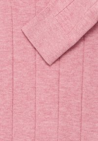 Rózsaszín bordázott kötött pulóver ujja egybe hajtva, amely megegyező textúrájú anyag háttérrel rendelkezik.