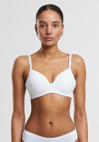 White padded bra with a deep V-neck design, thin adjustable straps, smooth texture, and seamless finish. Simple and minimalist style.
