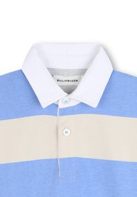 Πολύχρωμο μπλε και μπεζ πλεκτό μπλουζάκι με λευκό γιακά. Έχει κουμπιά στην μπροστινή πλευρά και μια ετικέτα που γράφει "BILLIEBLUSH" στον λαιμό.