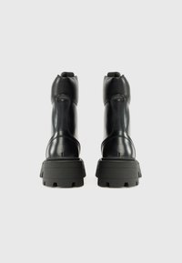 Bottines en cuir noir à finition brillante, dotées d'une semelle en caoutchouc noir épaisse et de coutures contrastées. Une paire conçue pour la durabilité.
