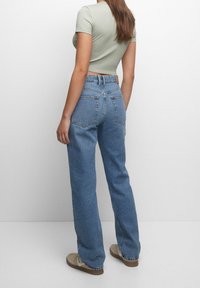 Højtaljede blå denimjeans med lige ben, der har baglommer og diskret slidmærkning. Kombineret med en tætsiddende lysegrøn top.