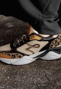 Sneaker beige e nera con un accento a stampa leopardata, tomaia in mesh testurizzato, dettagli in marrone a contrasto e una suola bianca scolpita.