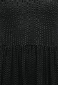 Black dress featuring vertical ribbed texture with small raised dots and a gathered skirt. Smooth top transitions to flowing pleats.