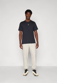 Melna īsām piedurknēm T-krekls ar nelielu logotipu, kopā ar gaiši pelēkiem sporta biksēm, uz sāniem ar uzrakstu "JORDAN", un sporta apaviem.