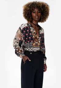 Langsleeve, collared shirt met een meerkleurig bloem- en geometrisch patroon op een zwarte achtergrond. Gemaakt van lichte stof, met een relaxte pasvorm.