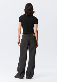 Black fitted t-shirt paired with wide-leg dark gray jeans. The jeans have a textured finish and visible back pockets. Leather patch at the waist.