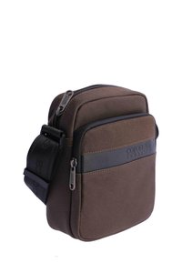 Bolso bandolera compacto de tela marrón con correa ajustable negra, dos compartimentos con cremallera y el logo "coronel tapicca" en el panel frontal.