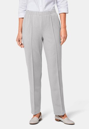 Lichtgrijze broek van een textuurstof, met een elastische tailleband en voorpijpen, gedragen met lichtgekleurde instap-schoenen.