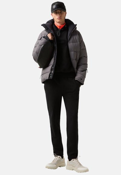 Puffjakke i grå, sort hættejakke og sorte sweatpants. Beige sneakers med strukturerede såler. Mørk kasket og lille sort taske tilføjer kontrast.