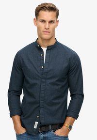Donkerblauwe, gestreepte overhemden met staande kraag en lange mouwen. Getextureerde stof met een zijlabel en gouden knopen.