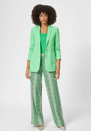Groene getailleerde blazer met twee voorzakken en gouden knopen, gecombineerd met geweven wijde broek in groene en zilveren tinten.