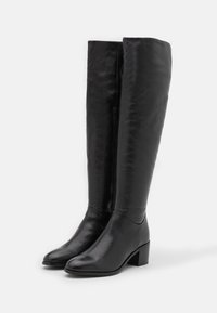 Botas negras de cuero hasta la rodilla con una textura suave, punta cuadrada y un tacón bajo de bloque. Cuentan con una cremallera lateral discreta para mayor facilidad de uso.