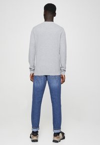 Gray long-sleeve sweater, loose fit, ribbed neckline; paired with light blue tapered jeans, rolled cuffs, and dark sneakers. Simple, casual outfit.