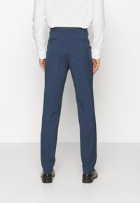 Navy blue trousers with a straight-leg design, two back pockets, and a smooth texture. Worn with a white long-sleeve shirt and black shoes.