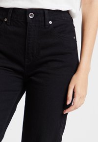 Höga svarta jeans i denim med en slät yta, klassisk femfickdesign och glänsande silverdetaljer.