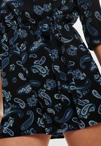 Černé šaty s paisley a květinovými vzory v odstínech modré a zelené. Mají stahovací pas a tříčtvrteční rukávy.