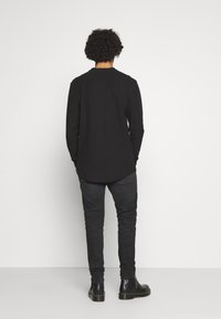 Camisa negra de manga larga con escote redondo, combinada con jeans ajustados gris y botas negras hasta el tobillo, vista desde la parte posterior.