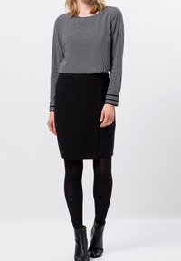 Schwarzer Rock mit Wickeldesign, kombiniert mit einem Langarmshirt mit strukturiertem grauen Muster und gestreiften Bündchen. Getragen mit schwarzen Strumpfhosen und ankle Boots.