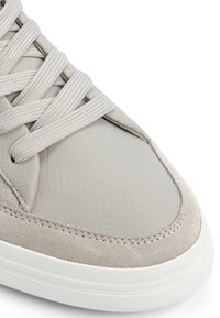 Zapatilla gris que presenta un upper de cuero texturizado, acentos de ante suave y cordones planos. Suela de goma blanca con detalles de costura.