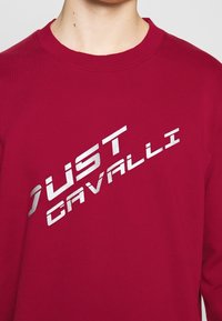 Rode katoenen sweatshirt met een ronde halslijn, voorzien van een metallic zilveren "JUST CAVALLI" logo over de voorkant in een diagonale lettertype.