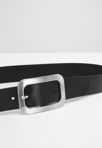 Ceinture en cuir noir avec une grande boucle rectangulaire en métal argenté. Elle dispose de trous pour le réglage et présente une texture lisse.