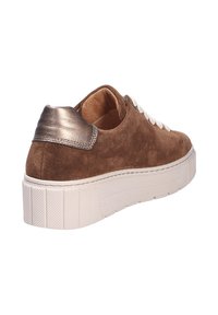 Bruine suède sneaker met een metallic zilveren hak, witte veters en een gestructureerde witte plateauzool. Achteraanzicht gefocust op het hakdetail.