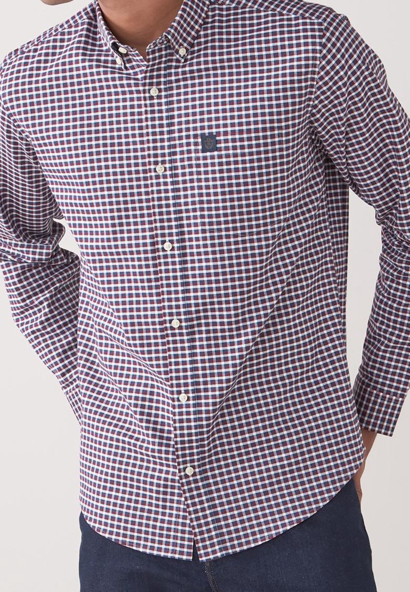 Homme portant une chemise à manches longues à carreaux bleu, blanc et rouge, associée à un pantalon bleu foncé.