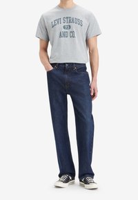 T-shirt gris avec l'impression "LEVI STRAUSS AND CO.", associé à un jean droit bleu foncé et des baskets noires avec des semelles blanches.