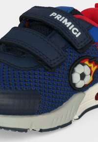 Μπλε παιδικό αθλητικό παπούτσι με ναυτικό λουράκια βέλκρο, κόκκινες και μπλε λεπτομέρειες και ένα σήμα με ποδοσφαιρική μπάλα με φλόγες στο πλάι.